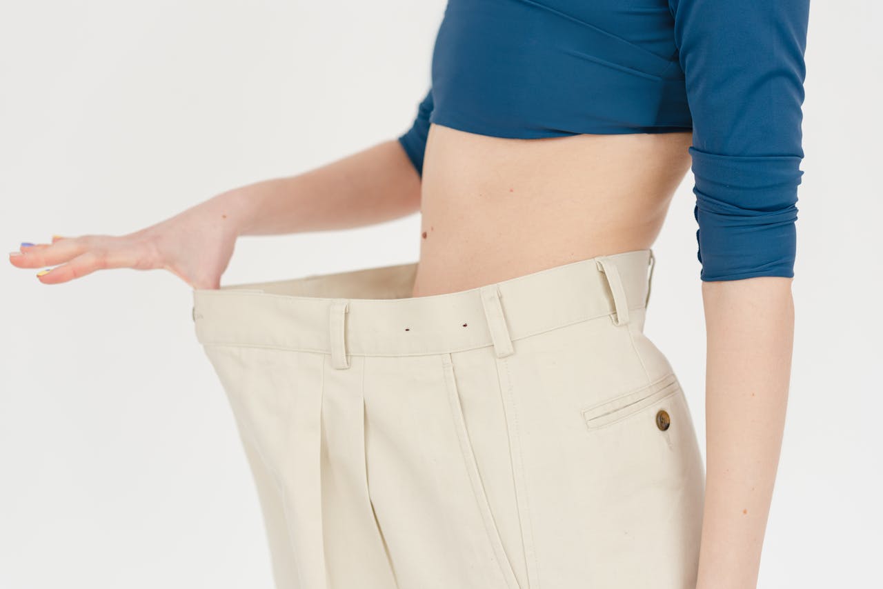 about-hero A woman demonstrates significant weight loss by wearing oversized pants indoors.