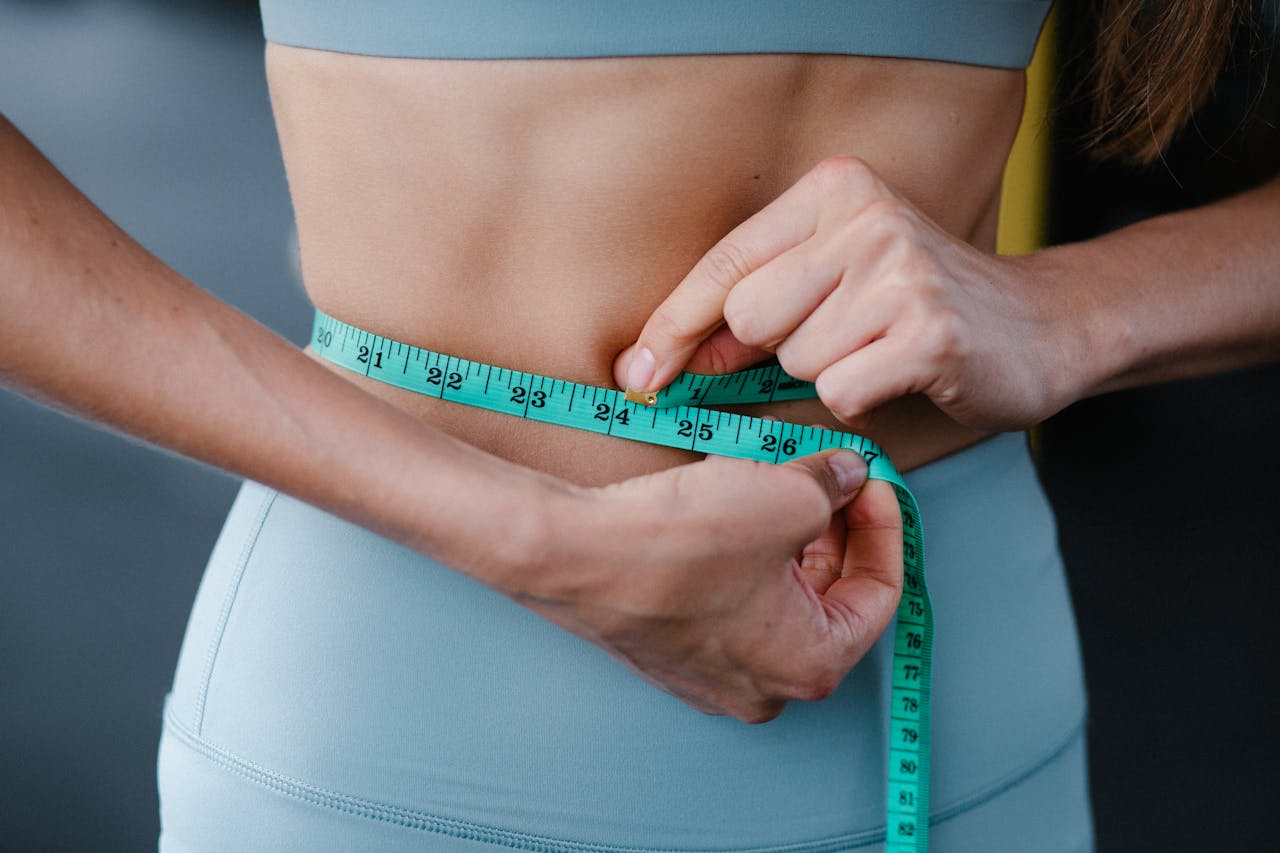who-we-are Close-up of a woman measuring her waist with a tape, representing fitness, health, and weight loss.